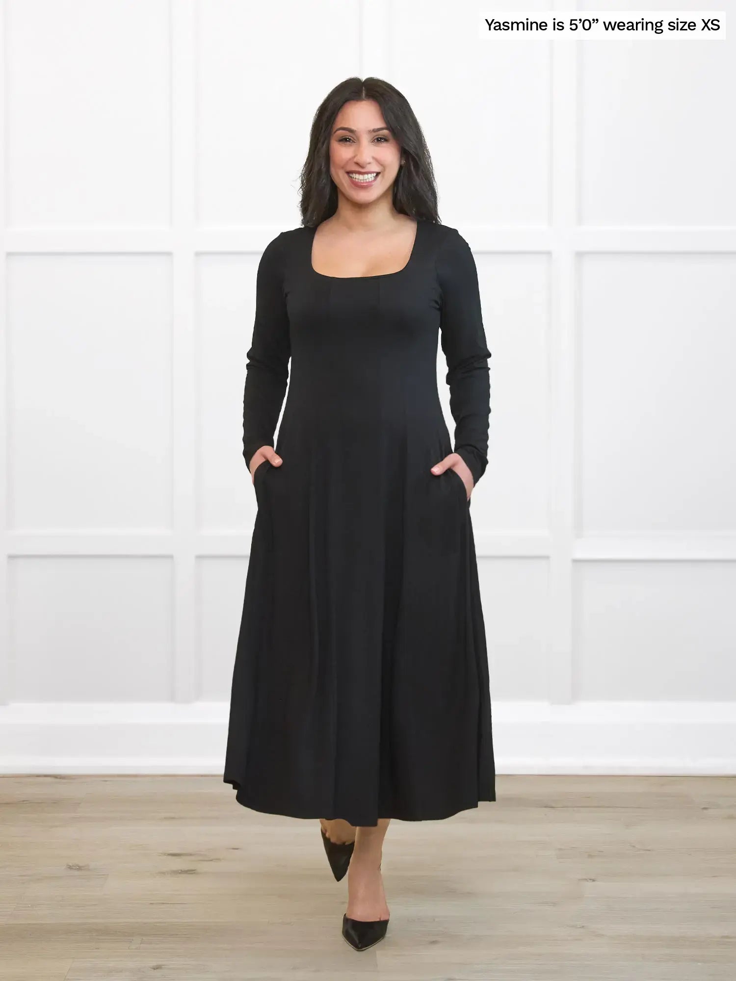 Woman wearing a black dress standing against a white wall.