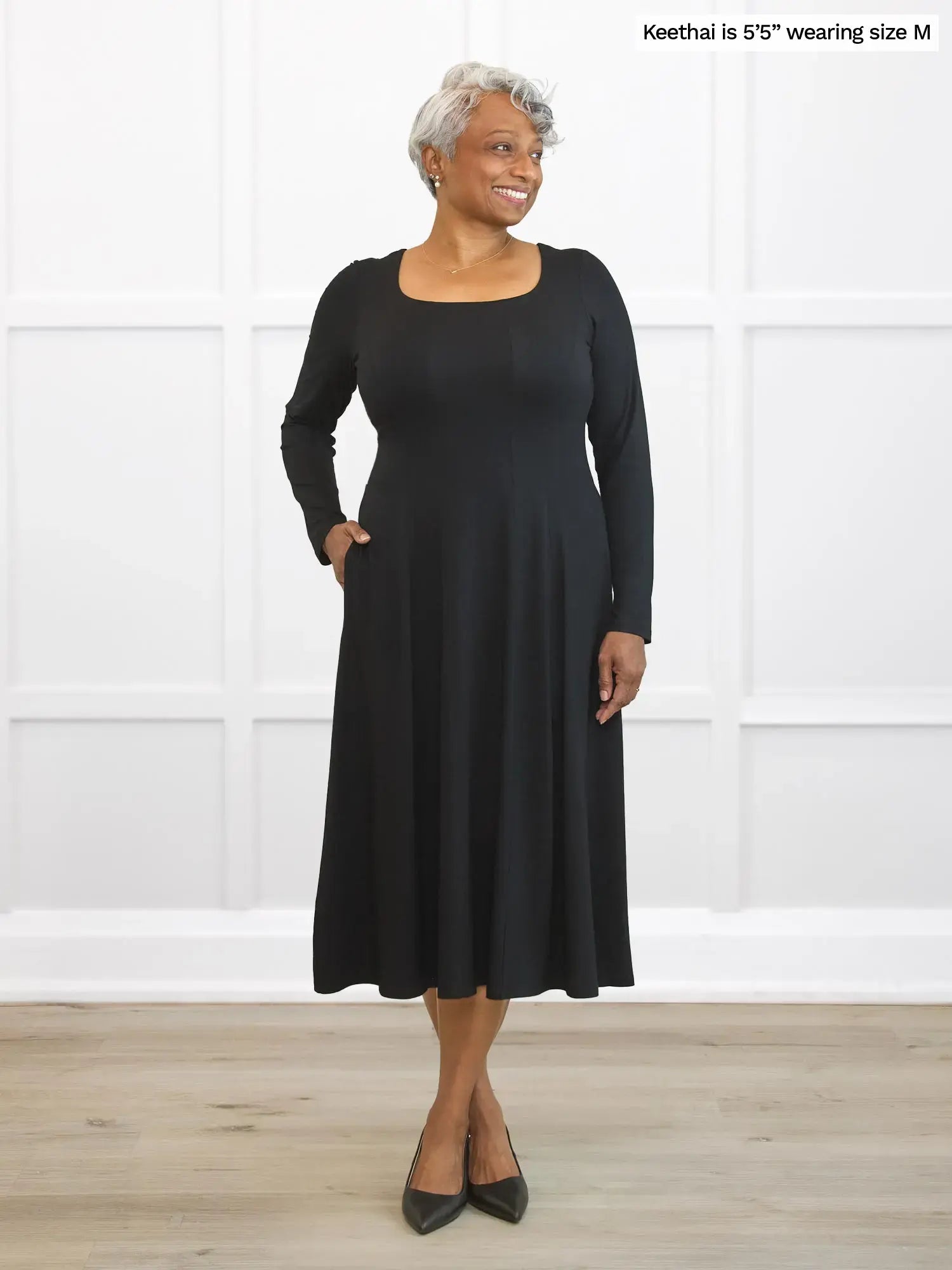 Woman wearing a black dress standing against a white wall.