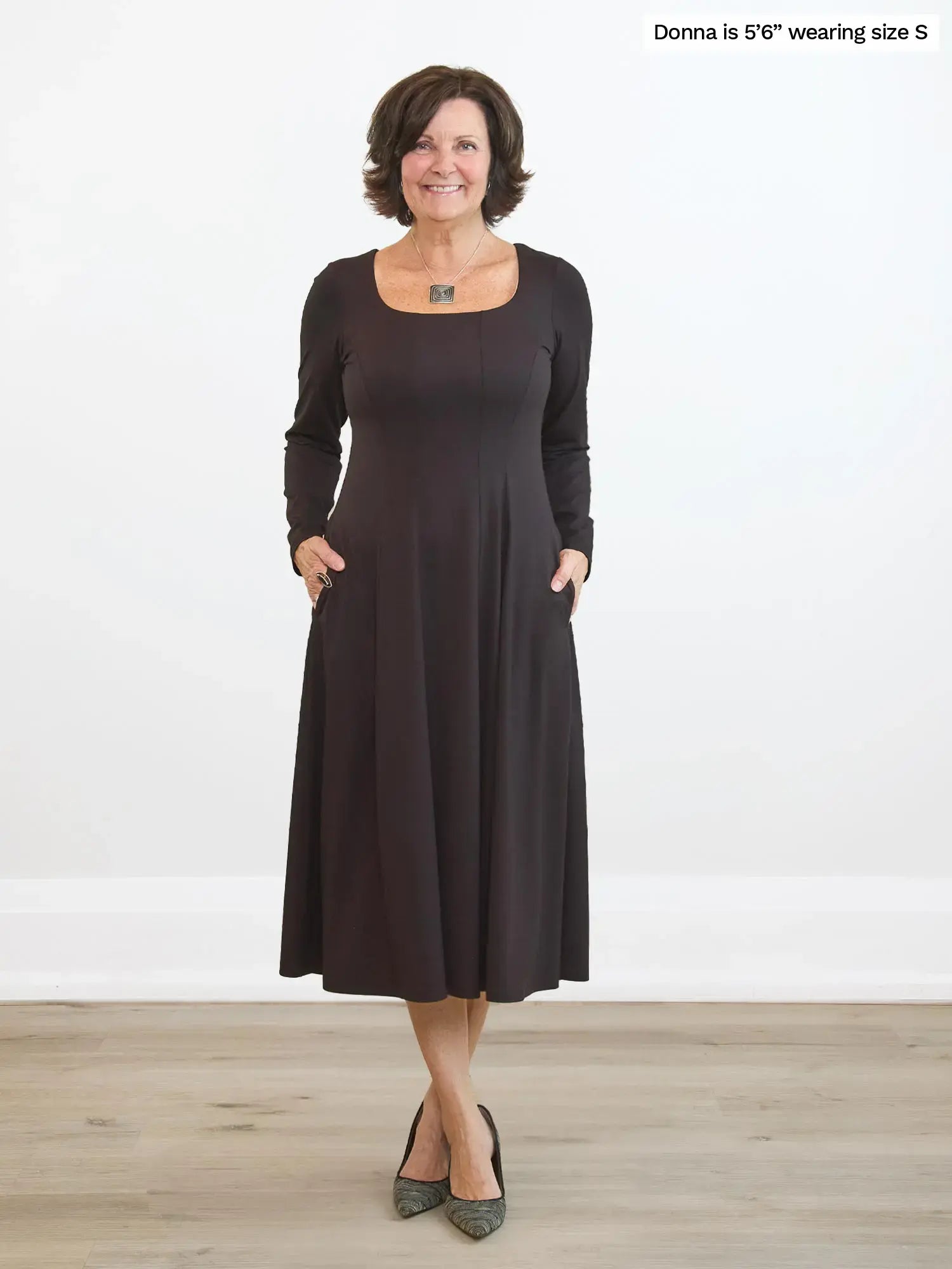 Woman wearing a dark brown dress standing on a wooden floor with a white background
