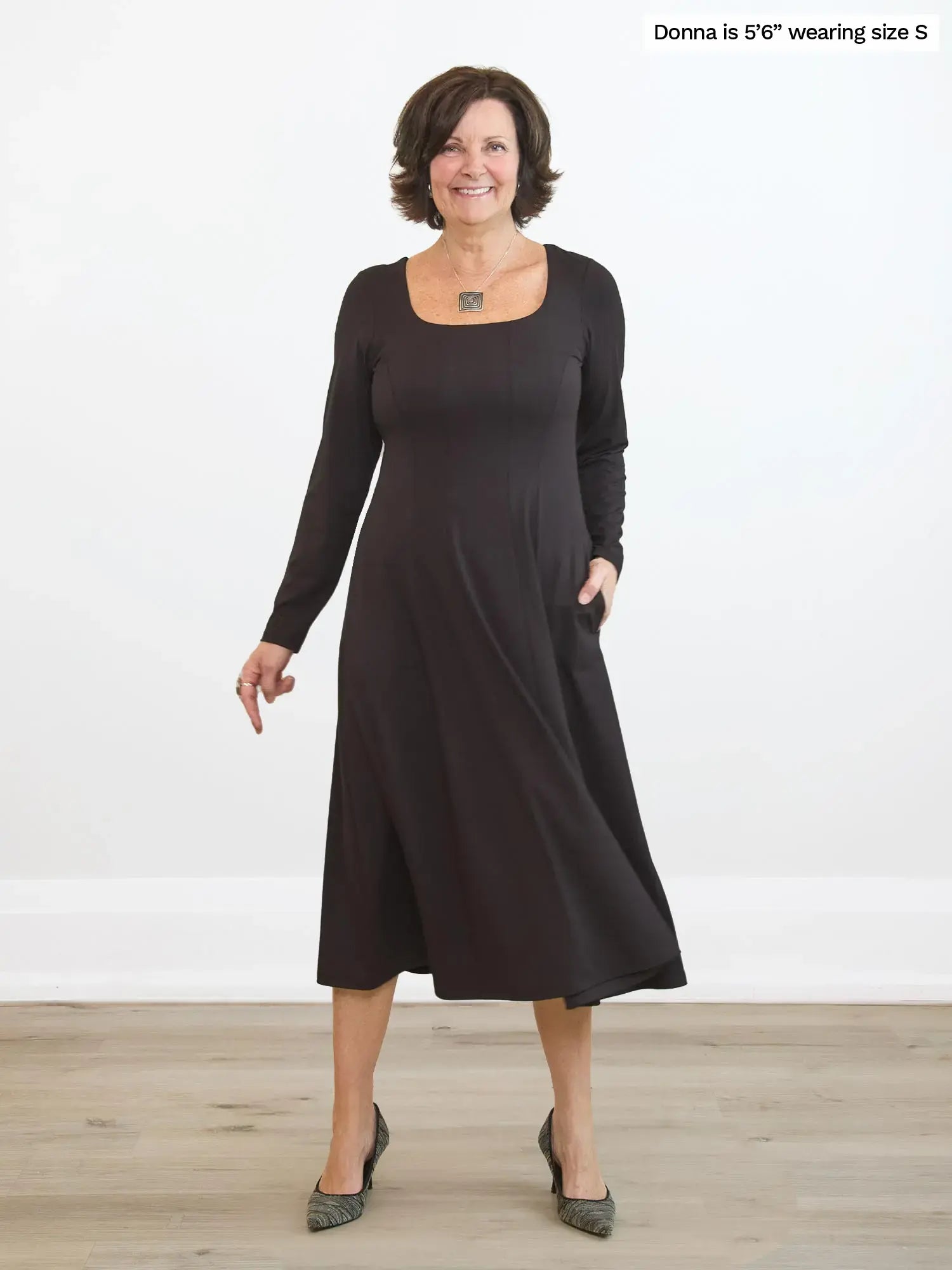 Woman wearing a dark brown dress standing on a wooden floor with a white background