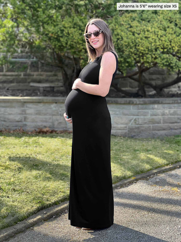 Miik model Jo (5'6", xsmall) standing sideway holding her pregnant belly wearing Miik's Prisha reversible maxi dress in black and sunglasses 