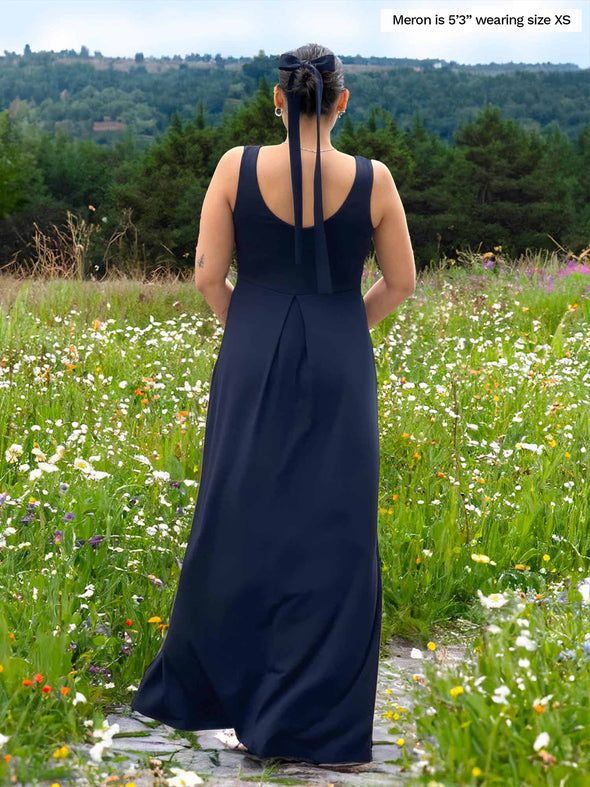 Miik model Meron (5’3”, xsmall) standing with her back towards the camera showing the back of Miik's Prisha reversible maxi dress in navy