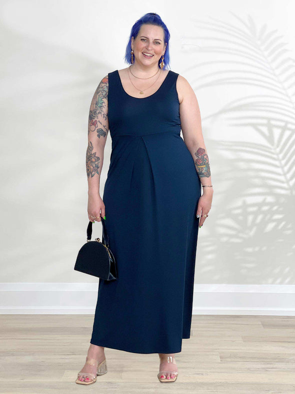 Miik model Kaitlin (5'9", xlarge) standing in front of a white wall wearing Miik's Prisha reversible maxi dress in navy