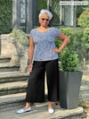 Woman standing in front of a house wearing Miik's Rio reversible dolman tee in blue ditsy print and black pants.