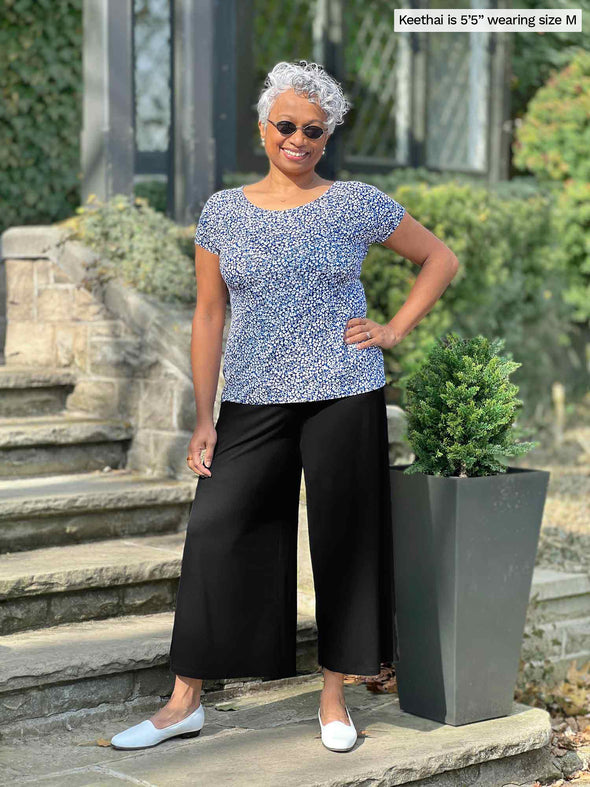 Woman standing in front of a house wearing Miik's Rio reversible dolman tee in blue ditsy print and black pants.