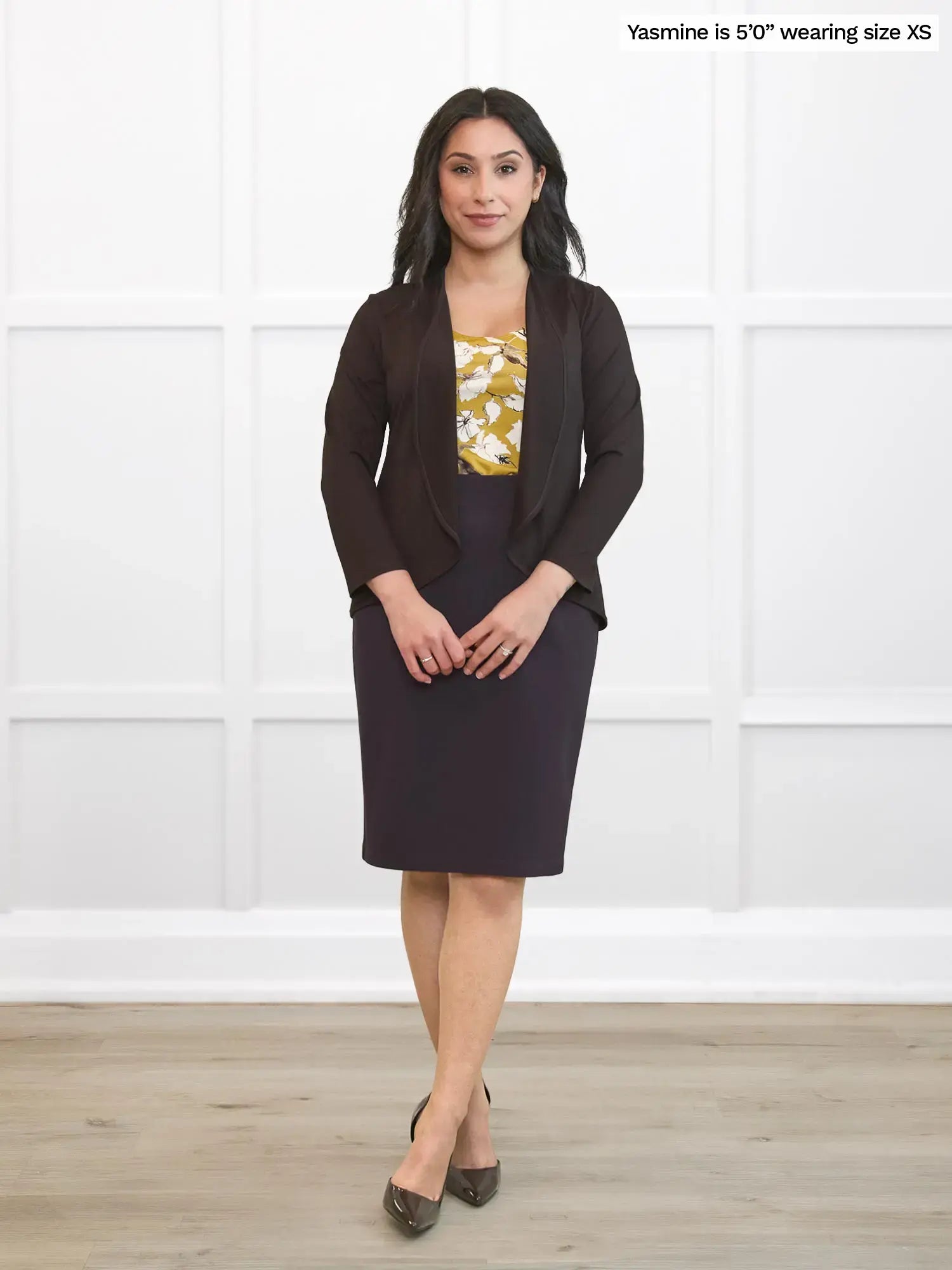 Woman wearing a dark brown cardigan and skirt with a yellow blouse featuring floral patterns against a white background