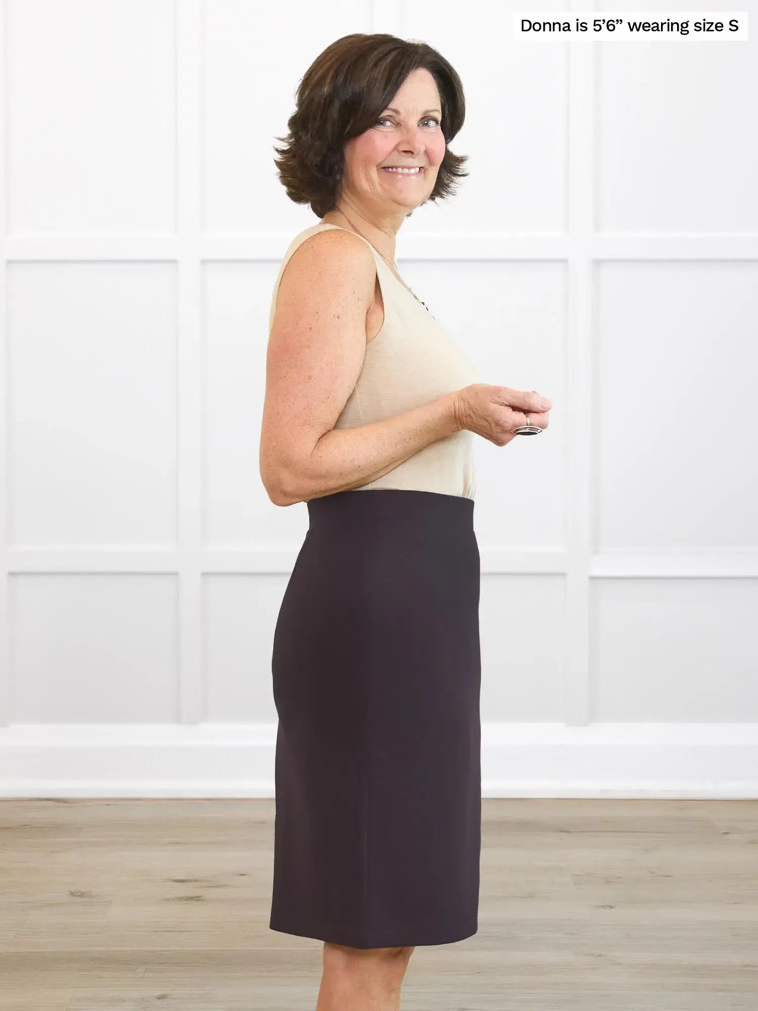 Woman wearing a beige top and dark brown skirt against a white background