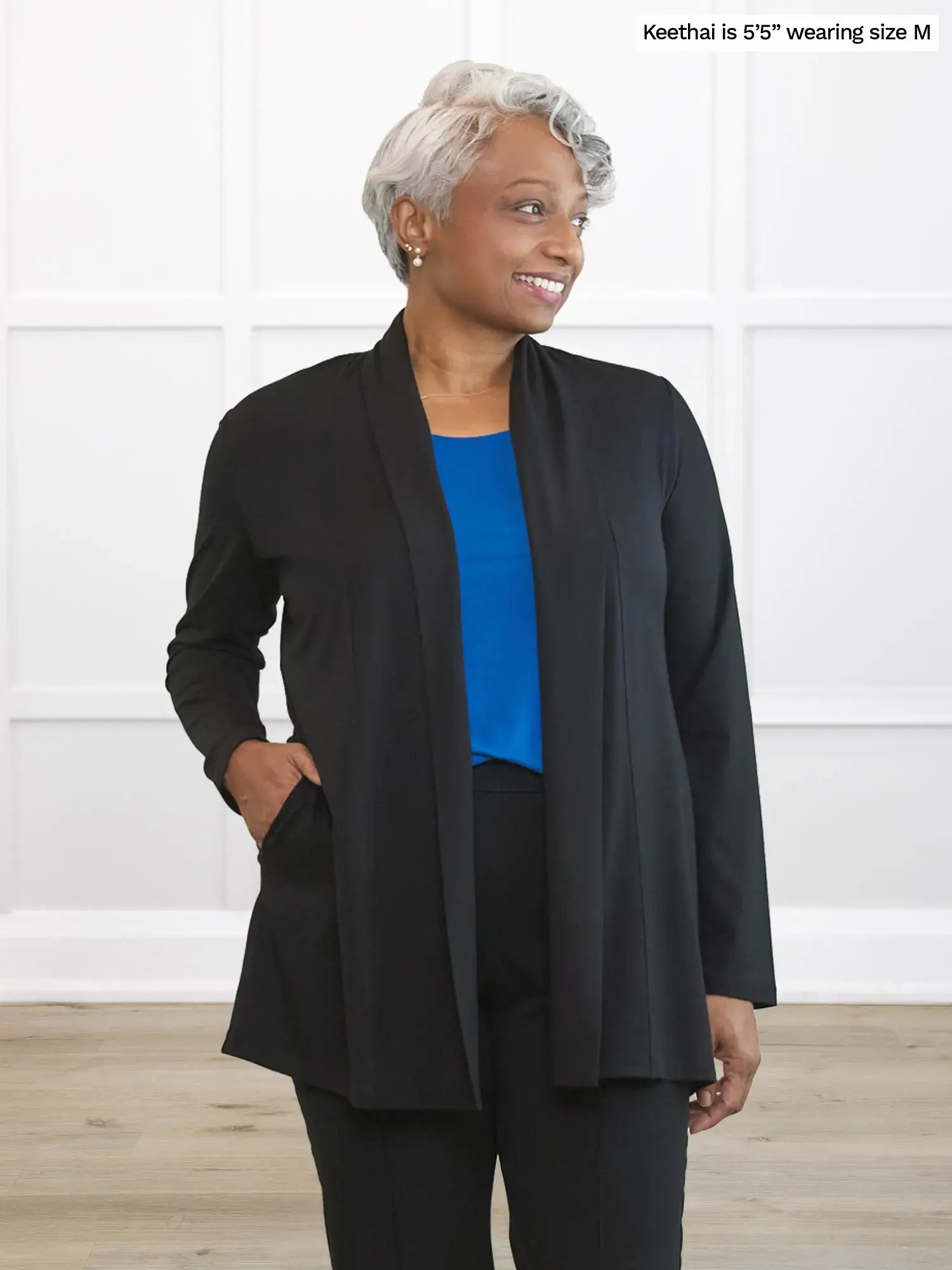 Woman wearing a black jacket over a blue top and black pants against a white background
