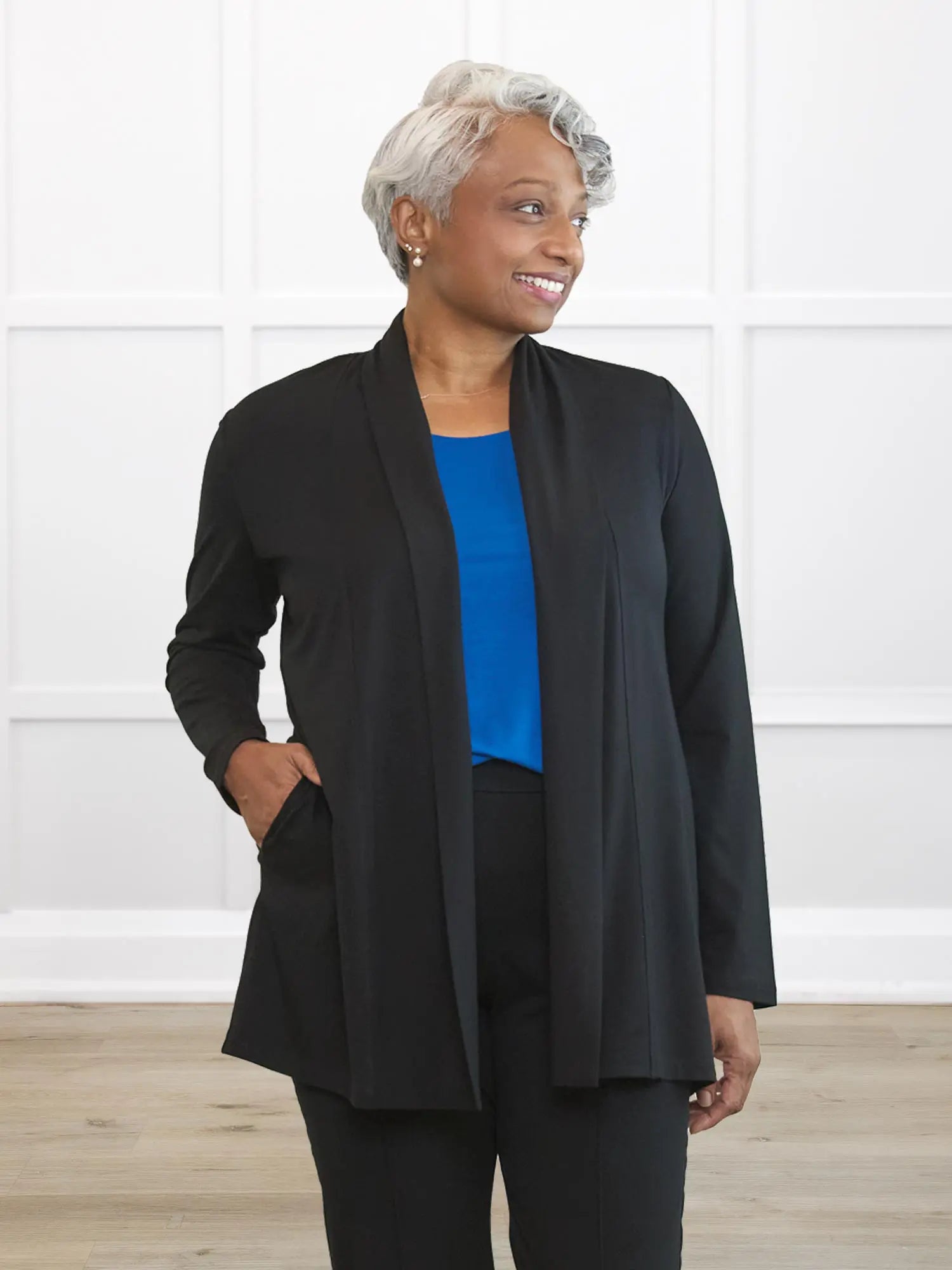 Woman wearing a black jacket over a blue top and black pants against a white background