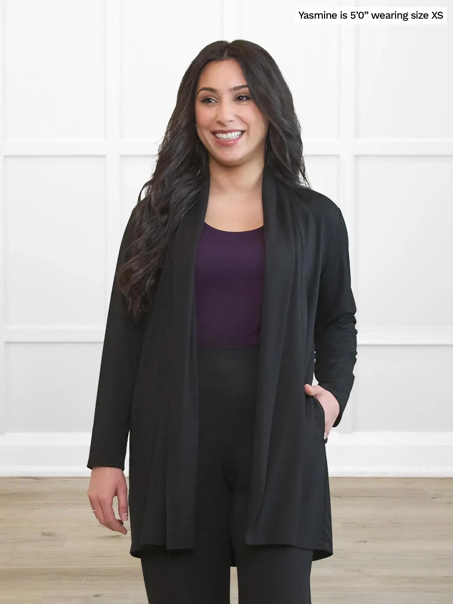 Woman wearing a black cardigan over a purple top and black pants on a white background