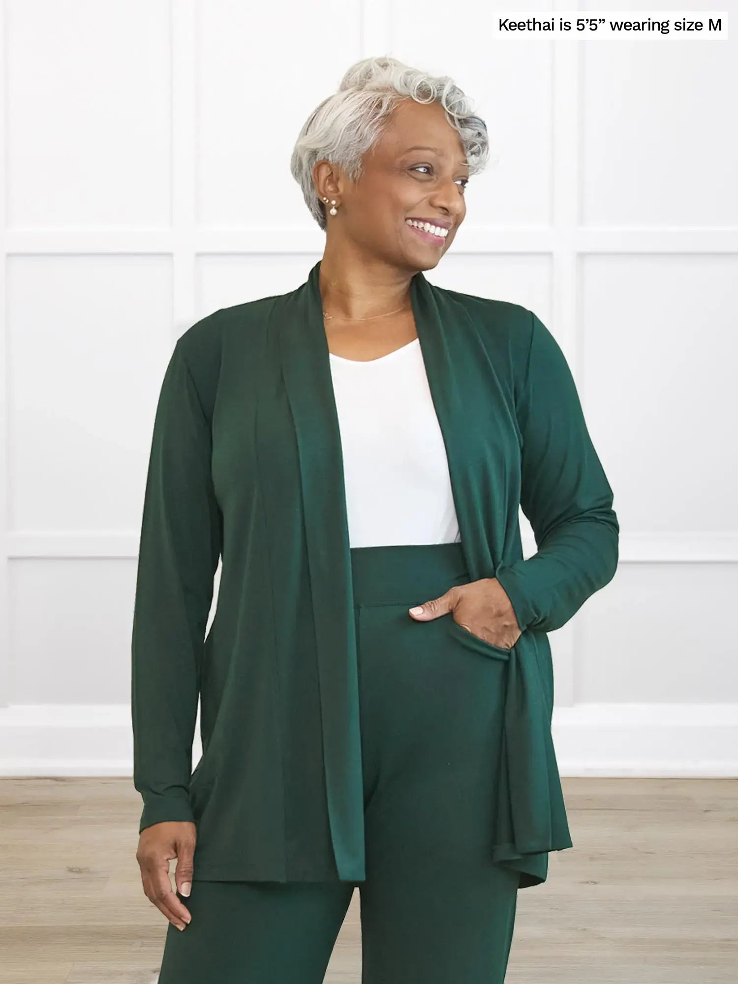 Woman wearing a green cardigan over a white tank top and matching green pants with a white background