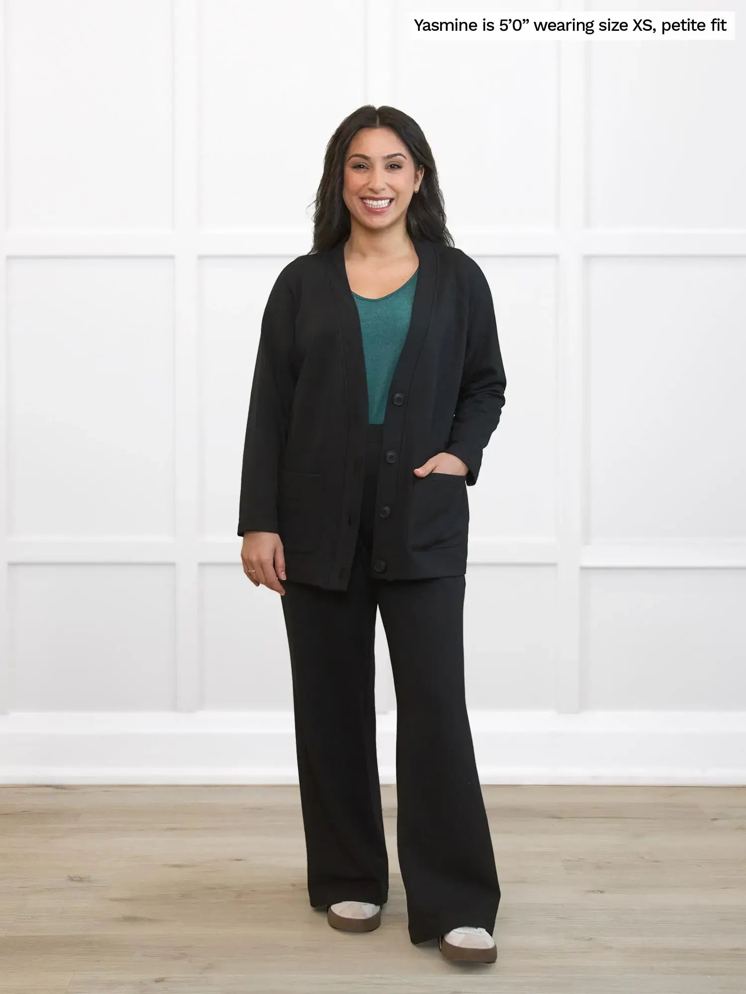 Woman wearing a black lounge set standing in a room with white walls and wooden floor.