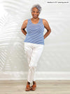Miik model Keethai. (5'5", medium) smiling while standing in front of a white wall wearing Miik's Shandra reversible tank top in cobalt mini stripe with white jeans 