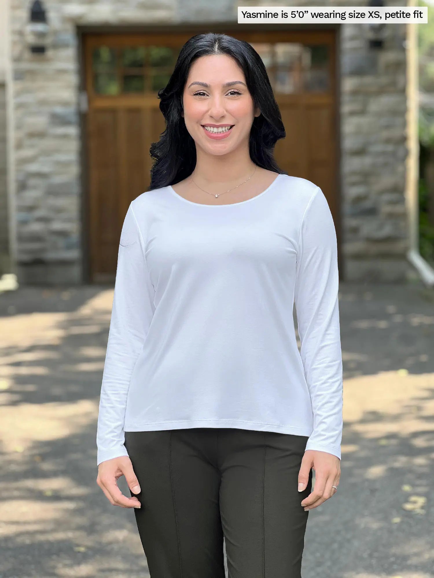 Miik model Yasmine (size XS) wearing the Shannon reversible long sleeve t-shirt in white, petite fit, with olive pants. She is wearing the round neckline side in the front, and the v-neck in the back.