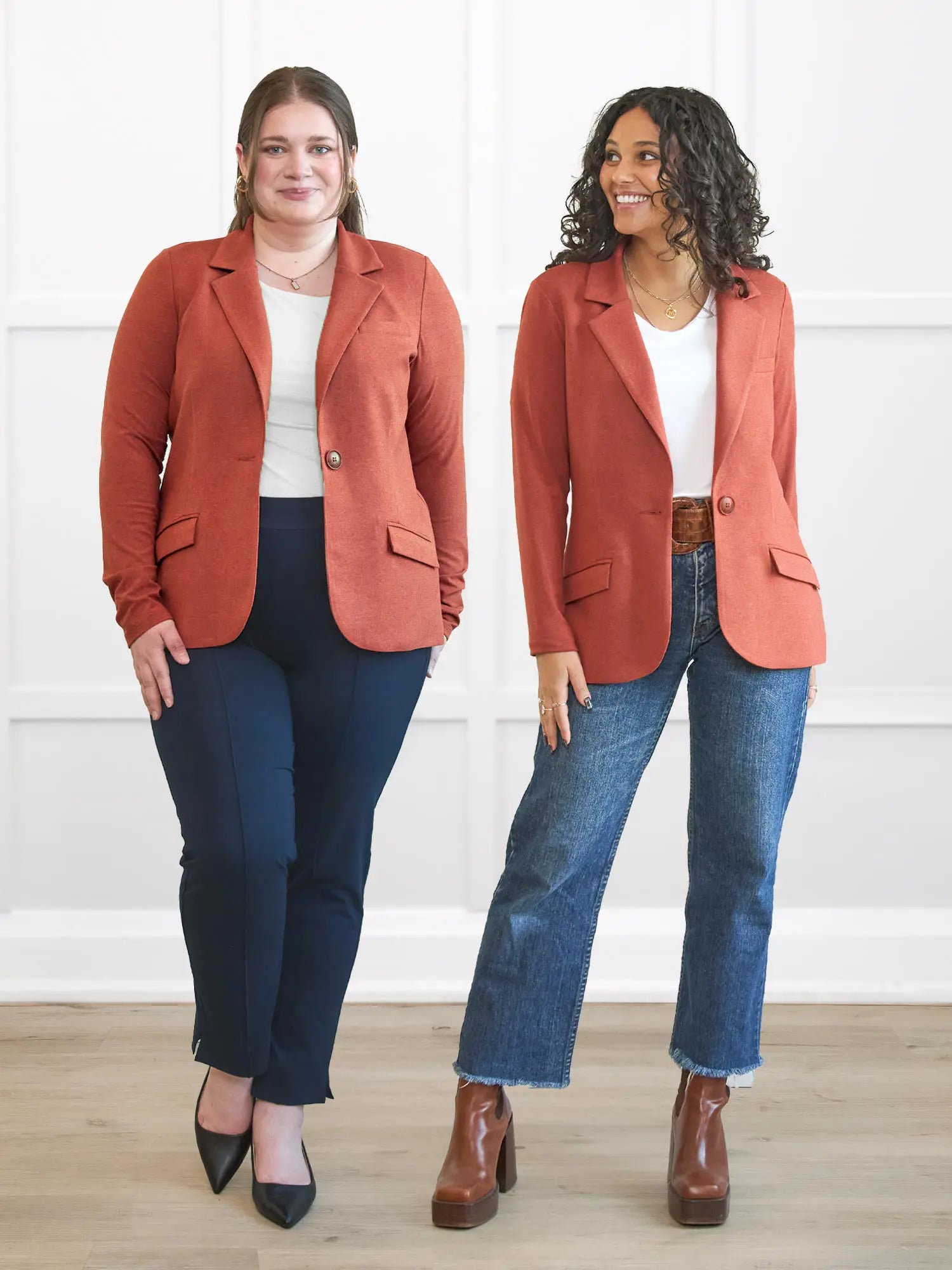 Two women wearing matching outfits with red blazers and blue jeans against a white wall