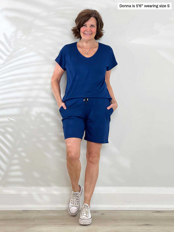 Miik founder Donna (5'6', small) smiling wearing Miik's Tanya short sleeve open-back romper in ink blue and white sneakers  
