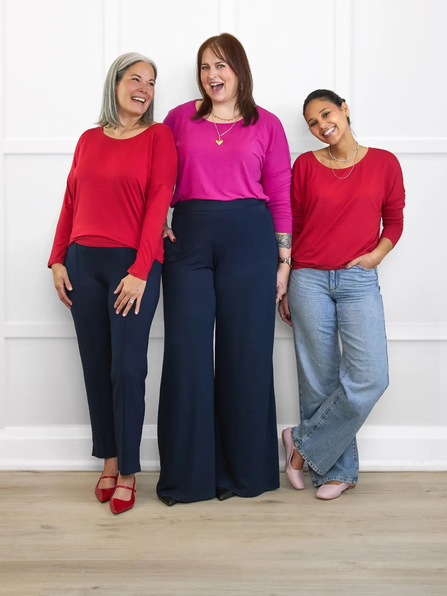 Three women standing together wearing colorful outfits against a white wall.