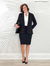 Miik founder Donna (5'6", small) smiling while leaning against to a white wall wearing a striped black skirt, a white collared top and Miik's Adette washable ponte blazer in black