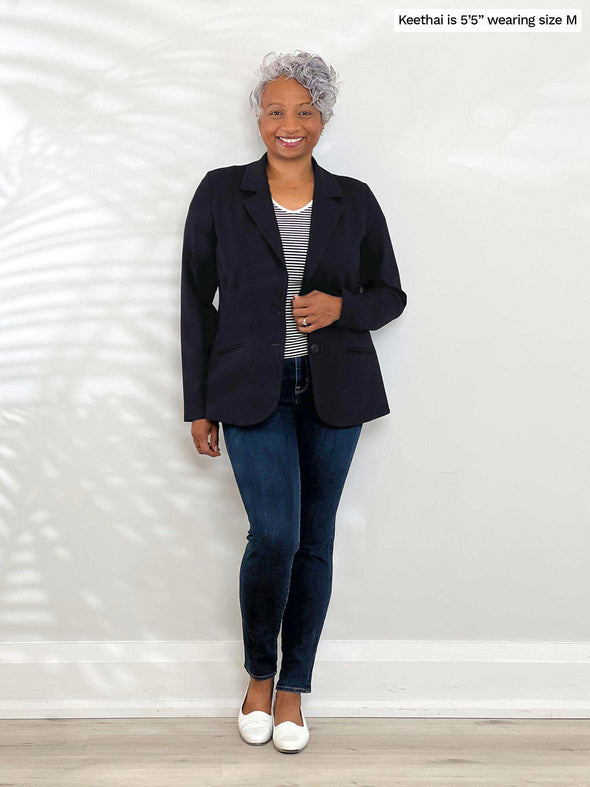 Miik model Keethai (5'5", medium) smiling while wearing Miik's Adette washable ponte blazer in black, a mini stripe tee and jeans 