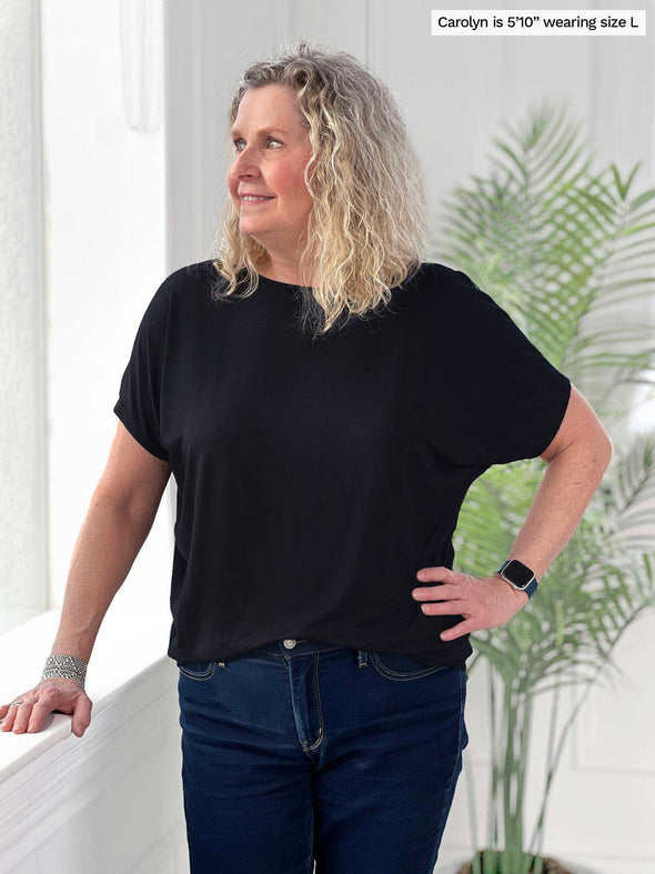 Miik model Carolyn (5'10", large) smiling and looking away wearing Miik's Adisa reversible dolman top in black with jeans 