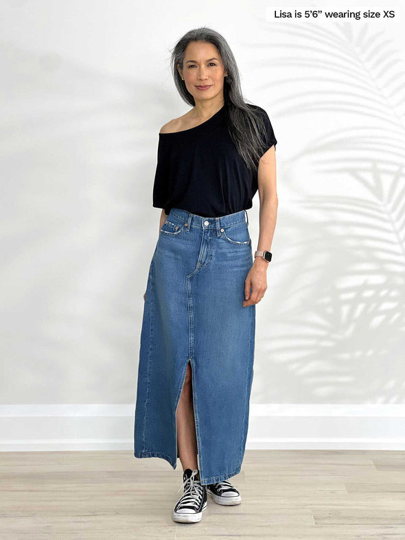 Miik model Lisa (5'6", xsmall) standing in front of a white wall wearing Miik's Adisa reversible slouchy dolman top in black with a long denim skirt 