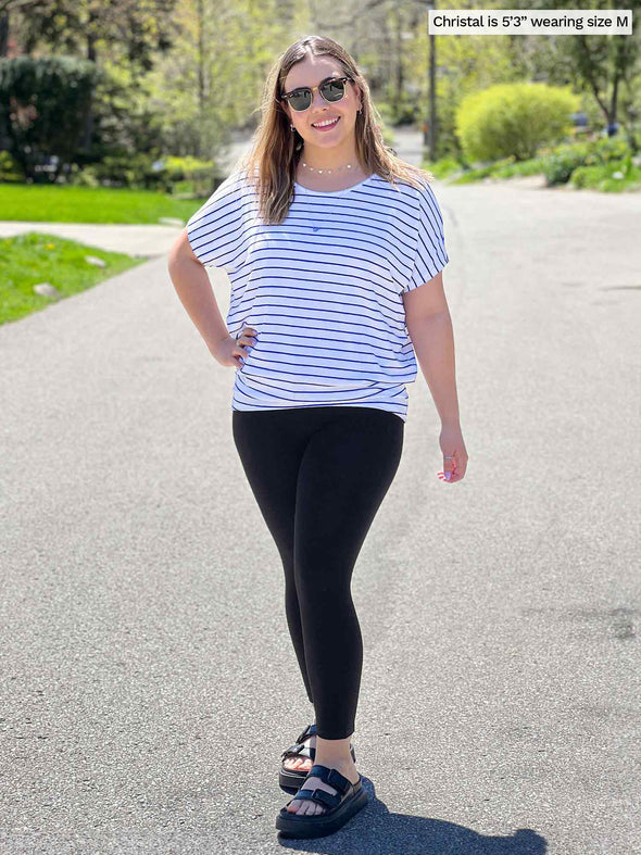 Miik model Christal (5'3", large) smiling while standing on a drive way wearing Miik's Adisa reversible slouchy dolman top in coastal stripe with a black legging 