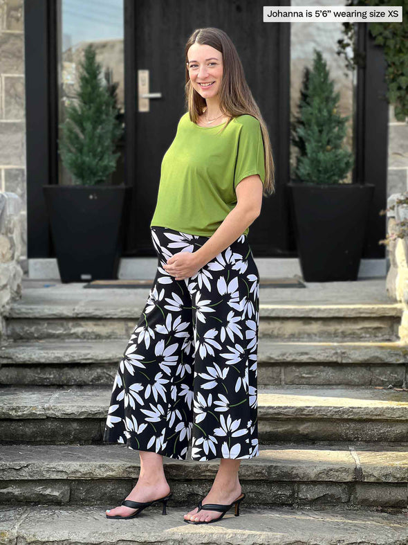 Miik model Jo (5'6", xsmall) smiling while standing sideway showing her pregnant belly wearing Miik's Adisa reversible dolman top in green moss along with a flare printed pant 