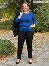 Miik model Christal (53", large) looking away and smiling wearing Miik's Akari side ruched reversible top in blueberry with a black jogger and a blazer over the shoulders 
