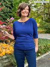 Miik founder Donna (5'6", small) smiling and looking away wearing jeans along with Miik's Akari side ruched reversible top in blueberry while holding a sunglass 