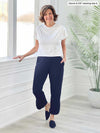 Miik founder Donna (5'6", small) smiling while standing next to a window/white wall wearing Miik's Akira tulip hem capri pant in navy with a white short sleeve top 