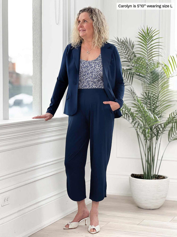 Miik model Carolyn (5'10", large) smiling and looking away wearing Miik's Akira tulip hem capri pant in navy with a matching colour blazer and a tank top in baby's breath print 