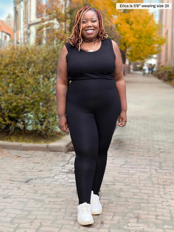 Miik model Erica (5'8", size 2x, plus size) smiling and looking away while wearing Miik's Alanis relaxed tank top in black and a legging in the same colour and white sneakers 