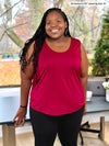 Miik model Kimesha (5'8", size 2x, plus size) smiling while leaning against to a desk wearing Miik's Alanis relaxed tank top in bordeaux with a black legging 