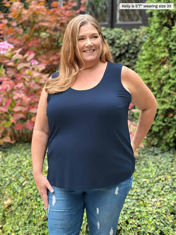 Miik model Kelly (5'7", size 3X, plus size) smiling and looking away wearing Miik's Alanis relaxed tank top in navy with jeans 