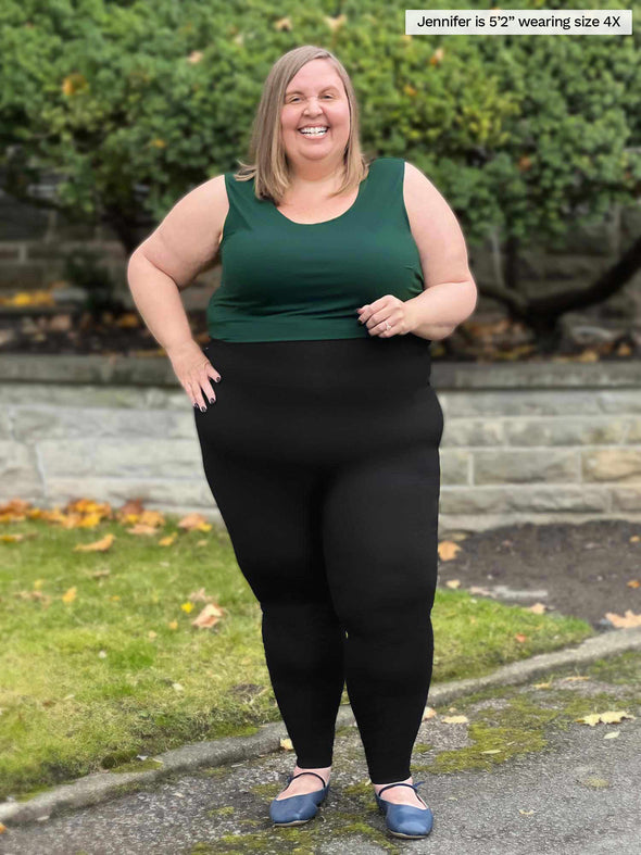 Miik model Jennifer (5'2", size 4X, plus size) smiling wearing Miik's Alanis relaxed tank top in pine green tucked in a black legging 