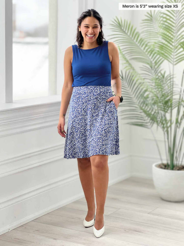 Miik model Meron (5'3". xsmall) smiling wearing Miik's Alara pocket swing skirt in baby's breath print with a tank top in ink blue 