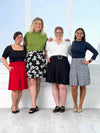 Miik models Mary-Ann, Carolyn, Bri and Meron standing next to each other, smiling, all wearing the new Miik skirt: the Alara pocket swing skirt. Colour available are: poppy red, white lily print, black, baby's breath and navy