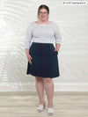Miik model Bri (5'5", xlarge) smiling wearing Miik's Alara pocket swing skirt in navy with a striped 3/4 sleeve top 