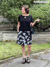 Miik founder Donna (5'6", small) looking away and smiling wearing Miik's Alara pocket swing skirt in white lily with a black tee 