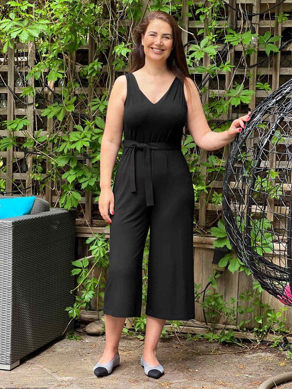 Woman standing outside smiling while wearing Miik's Alice reversible capri wide leg jumpsuit in black. 