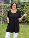 Miik founder Donna (5'6", small) smiling wearing Miik's Alma half sleeve pocket tunic in black with white jeans 