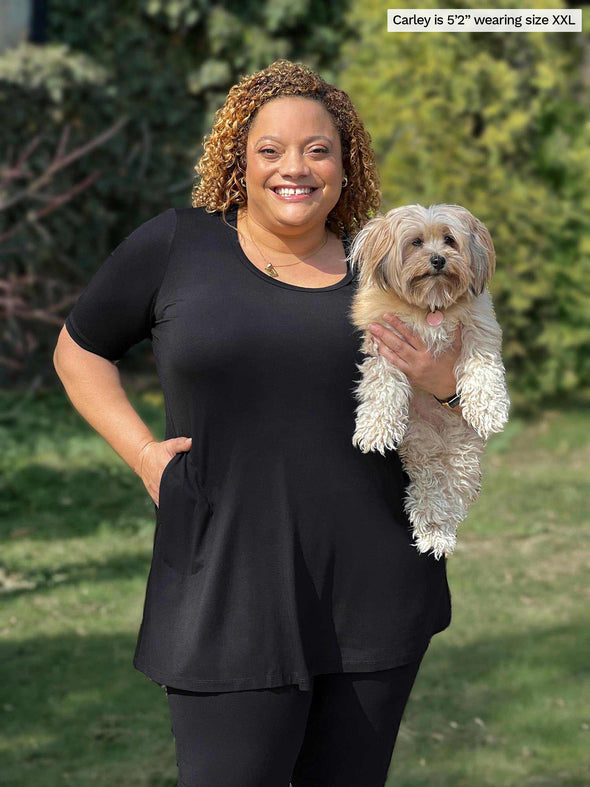 Miik model Carley (5'2", xxalrge) smiling while holding a puppy wearing an all black outfit: Miik's Alma half sleeve pocket tunic and Lisa2 high waisted legging 