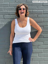 Miik founder Donna (5'6", small) laughing while leaning against to a brick wall wearing Miik's Amina reversible shelf bra tank in white and navy pant 