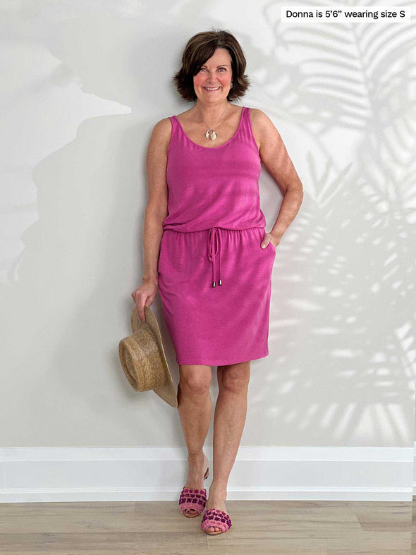 Miik founder Donna (5'6", small) smiling while standing in front of a white wall wearing Miik's Amy drawstring pocket dress in pink