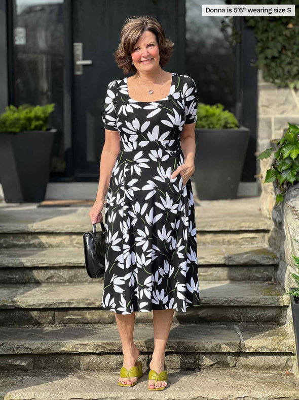 Miik founder Donna (5'6", small) wearing Miik's Anika puff sleeve midi dress in white lily print holding a black purse