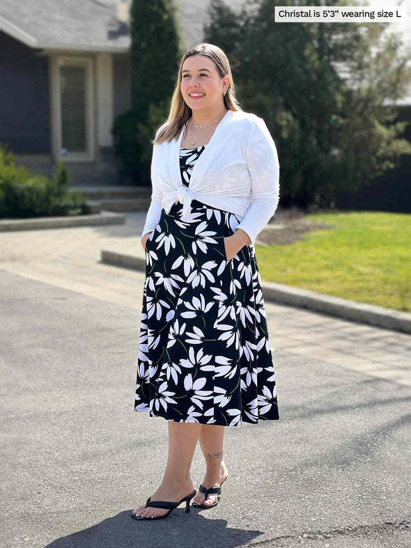 Miik model Christal (5'3", large) smiling and looking away wearing a white cardigan tied with Miik's Anika puff sleeve midi dress in white lily print
