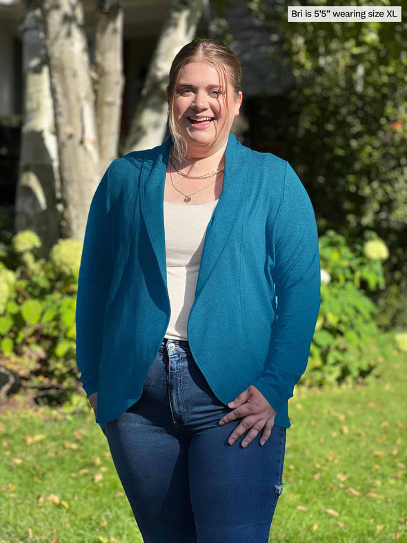 Miik model Bri (5'5", xlarge) smiling while wearing Miik's Anne soft stretch blazer in teal melange, a white tank and jeans