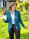 Miik founder Donna (5'6", small) looking away and smiling wearing a collared shirt in white along with Miik's Anne soft stretch blazer in teal melange and a dressy black pant