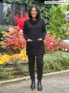 Miik model Meron (5'3", xsmall) laughing with hands on the front pocket wearing a black jogger with Miik's 		Ashanti long sleeve cowl neck pocket tunic in the same colour 