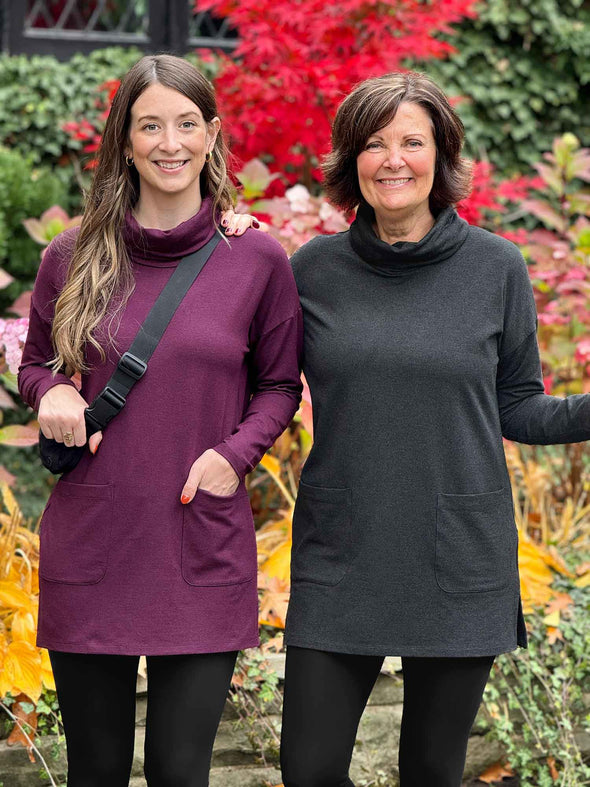 Miik model Jo and founder Donna standing next to each other smiling both wearing Miik's 		Ashanti long sleeve cowl neck pocket tunic. Jo is wearing the tunic in port melange and Donna in charcoal. They are both matching them with a black legging 